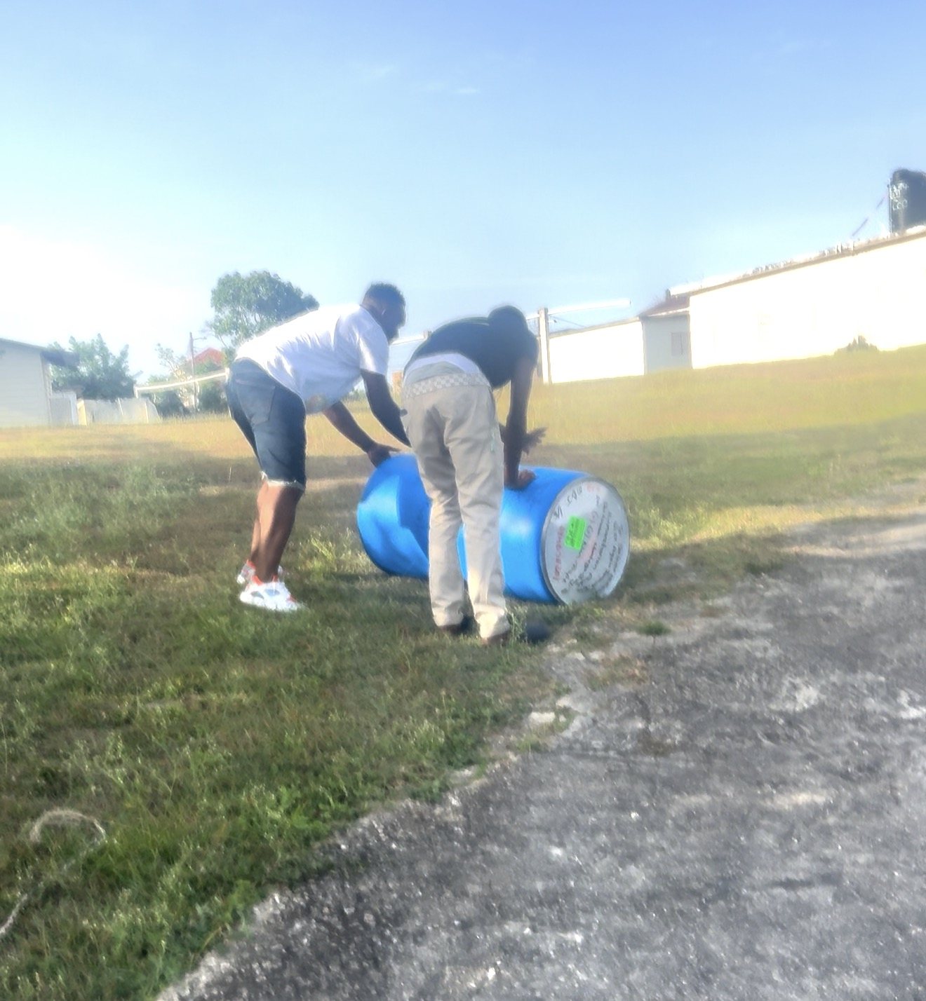 Two men rolling a Rise Again Jamaica Incorporated aid barrel across the churchyard in Prospect, Trelawny.