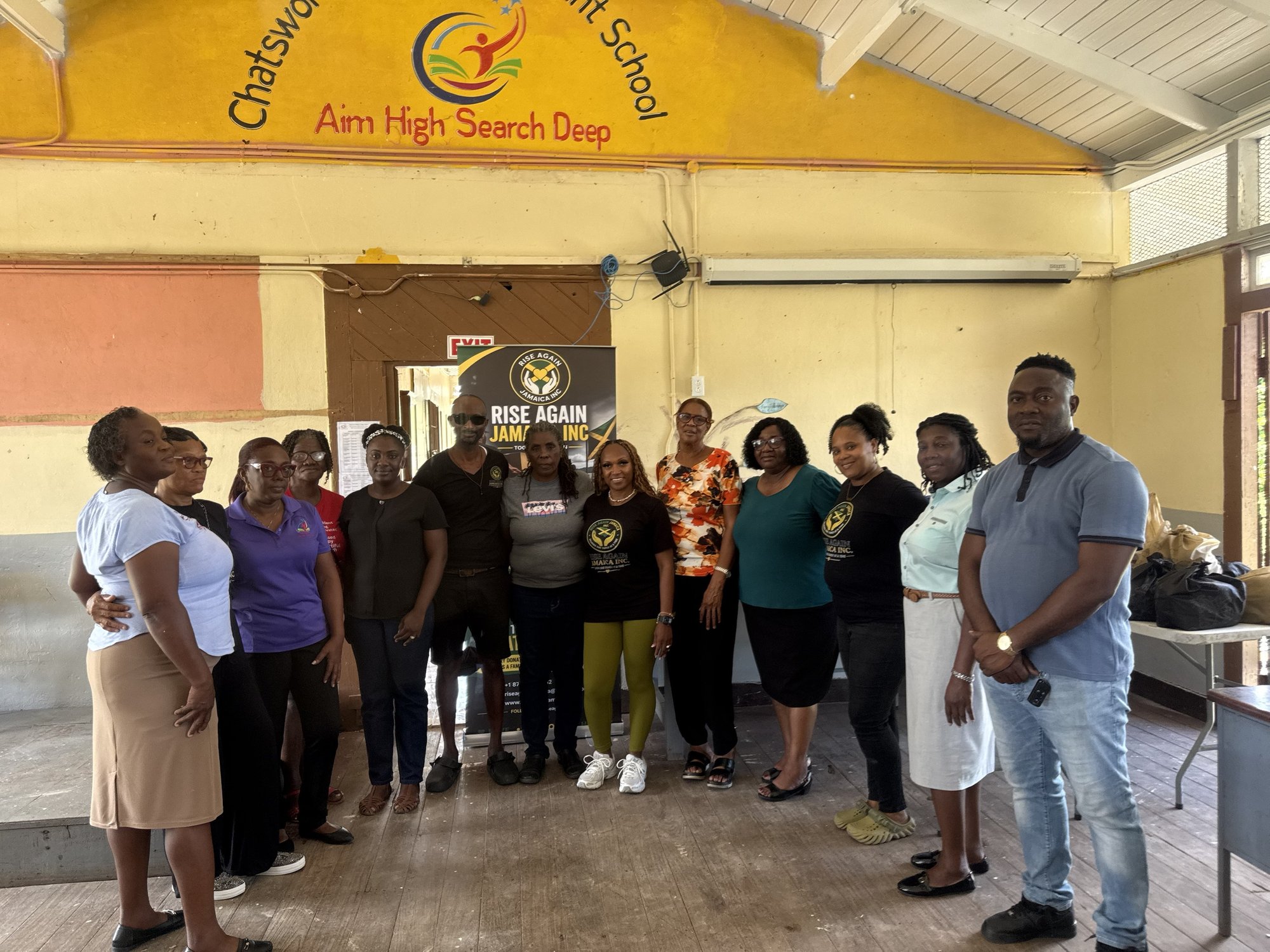 School staff and the Rise Again Jamaica Incorporated team standing together in the school hall.