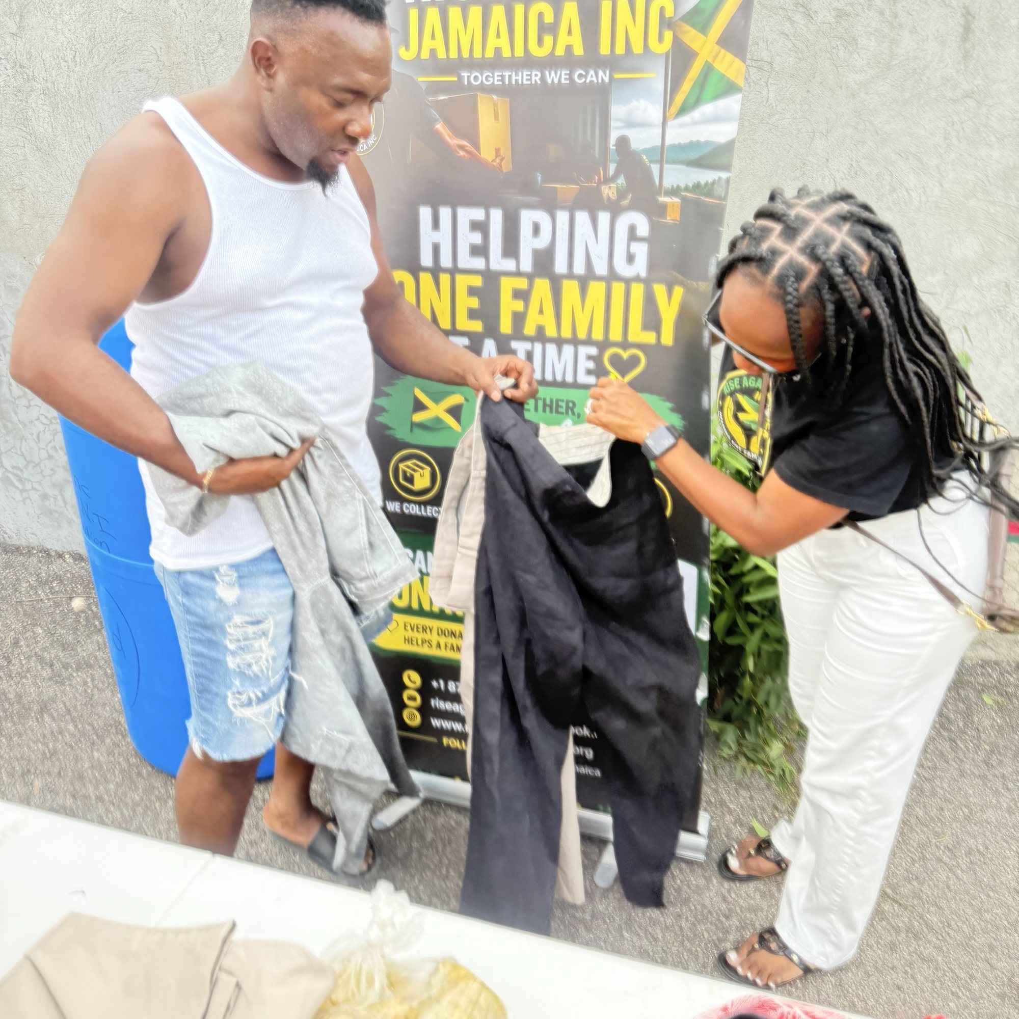 Michelle Ramundo handing clothing to a resident at the Mount Salem distribution, beside the Rise Again Jamaica Incorporated banner.